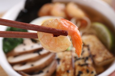 Photo of Chopsticks with shrimp above bowl of ramen, closeup. Noodle soup