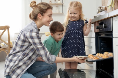 Photo of Mother and her children taking out cookies from oven in kitchen