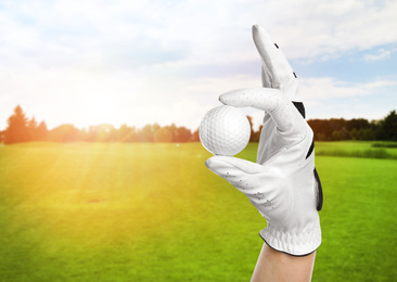 Player holding golf ball in park on sunny day, closeup. Space for design