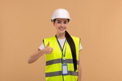 Engineer with hard hat and badge showing thumb up on beige background