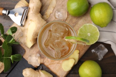 Photo of Glass of tasty ginger ale with ice cubes and ingredients on wooden table, flat lay