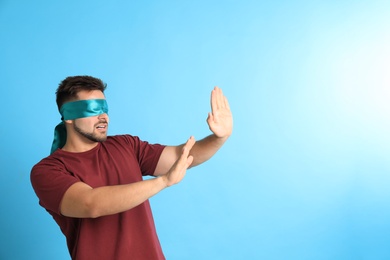 Young man with blindfold on blue background, space for text
