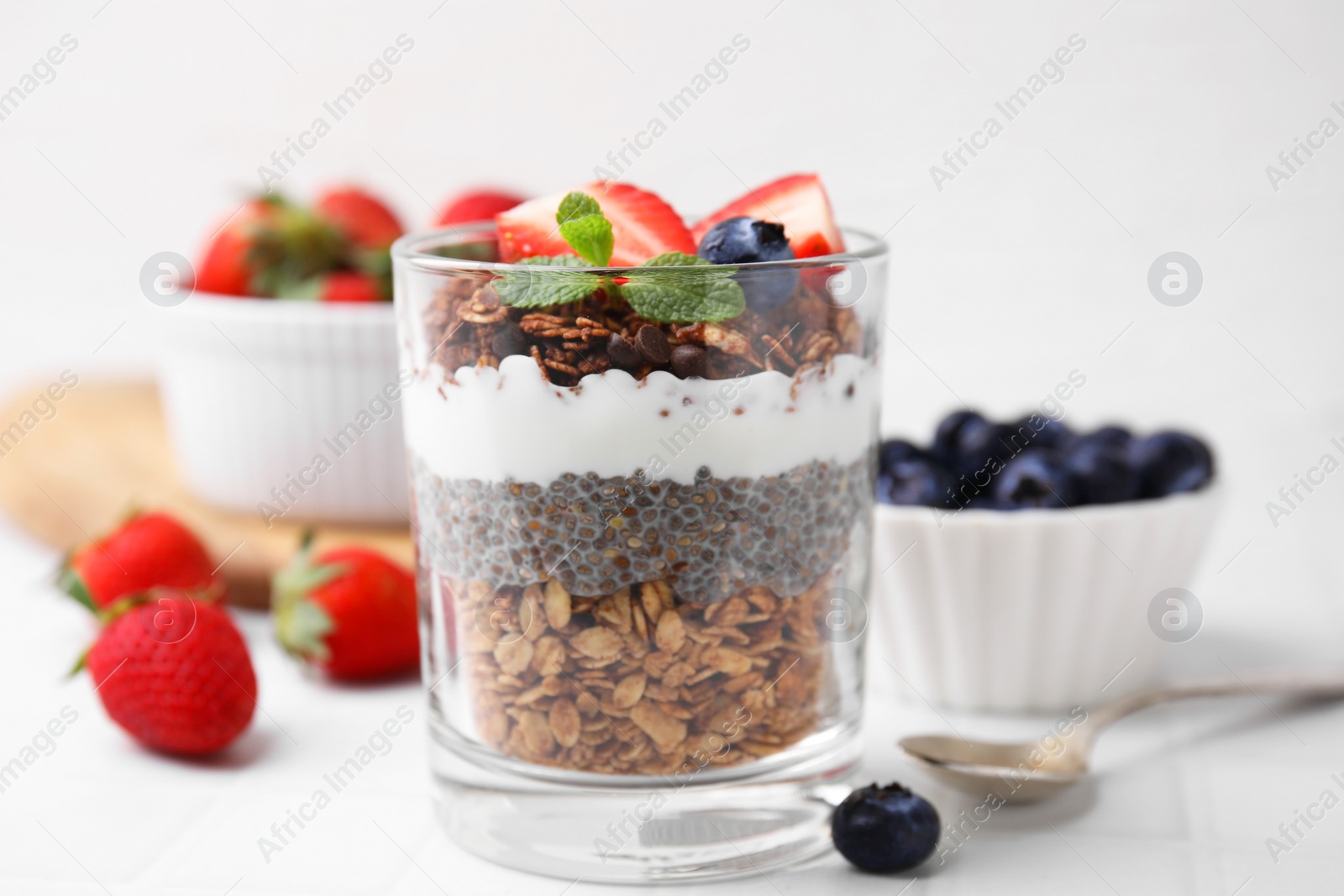 Photo of Tasty granola with berries, yogurt and chia seeds in glass on white table