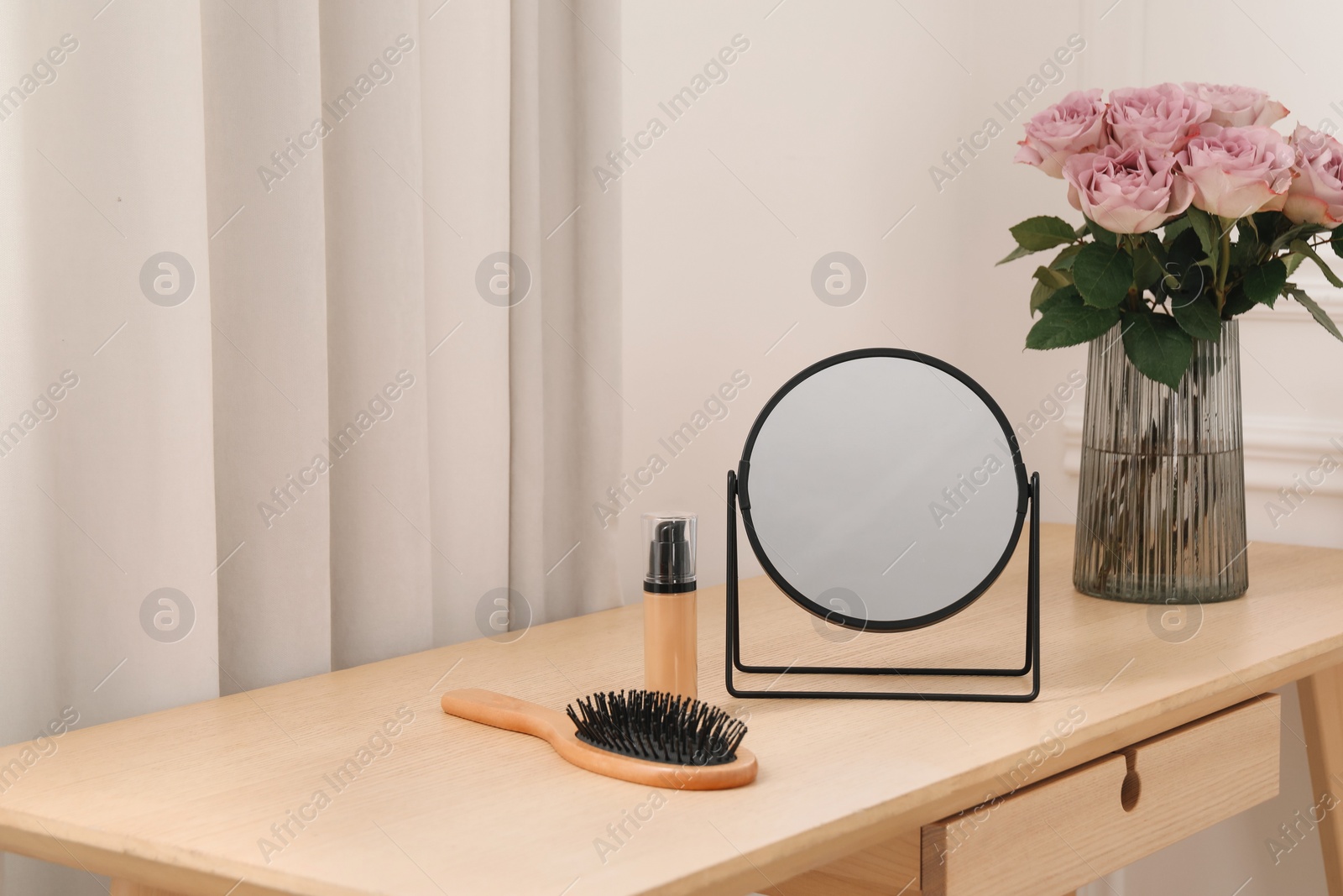 Photo of Mirror, foundation, brush and vase with pink roses on wooden dressing table in makeup room, space for text
