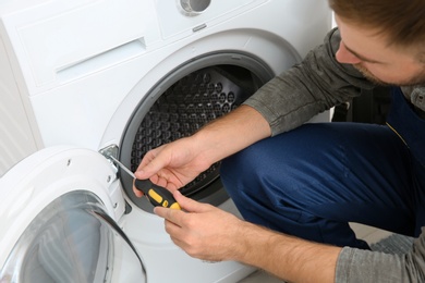 Young plumber fixing washing machine in bathroom