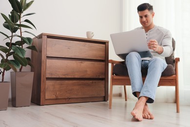 Photo of Man with laptop sitting in armchair at home. Floor heating system