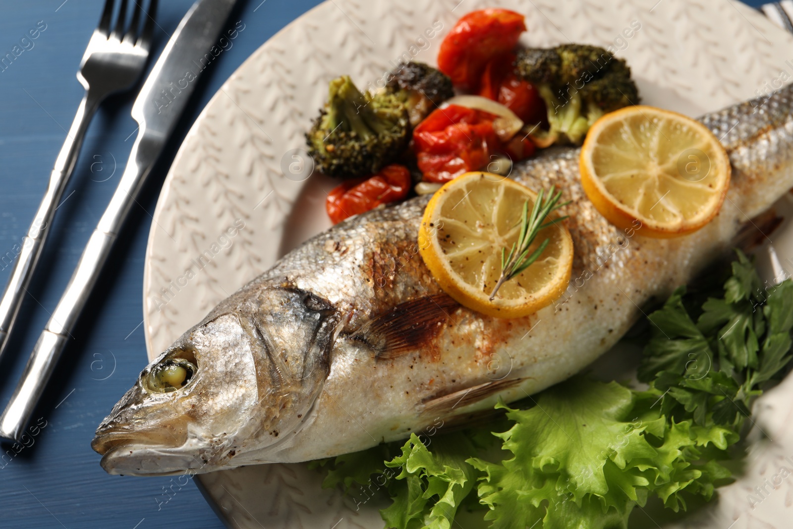 Photo of Delicious baked fish and vegetables served on blue wooden table, closeup