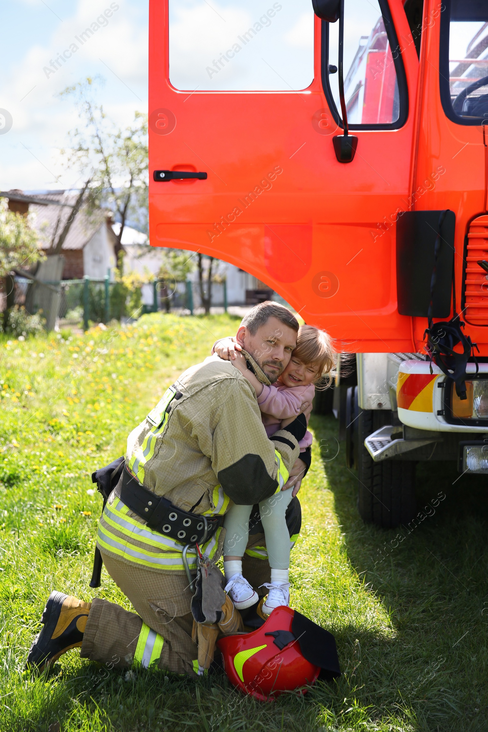 Photo of Firefighter in uniform with rescued little girl near fire truck outdoors. Save life