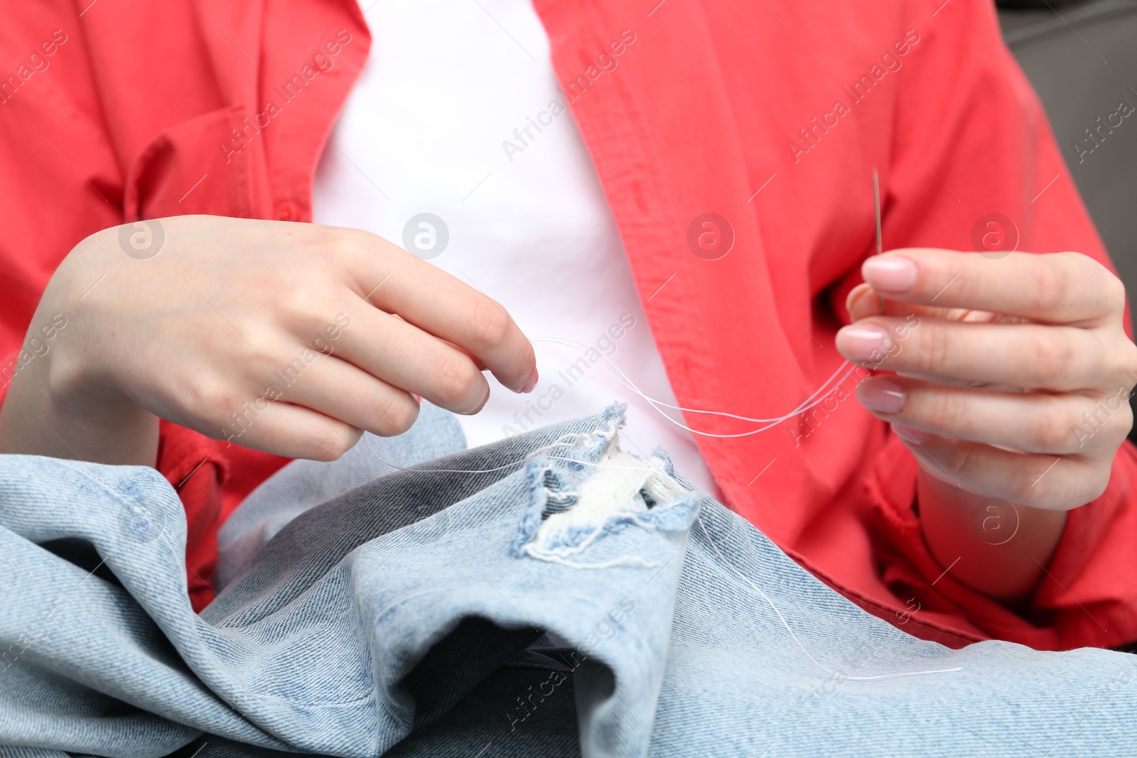 Photo of Woman sewing jeans with needle, closeup view