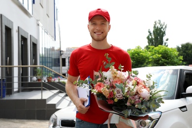 Delivery man with beautiful flower bouquet near car outdoors