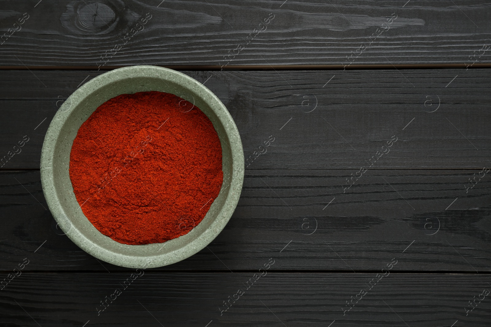 Photo of Bowl of aromatic paprika on black wooden table, top view. Space for text
