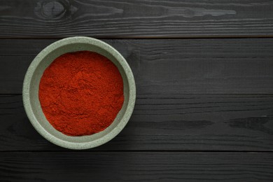 Bowl of aromatic paprika on black wooden table, top view. Space for text