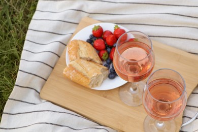 Photo of Glasses of delicious rose wine and food on picnic blanket outdoors