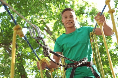 Photo of African-American teenage boy climbing in adventure park. Summer camp