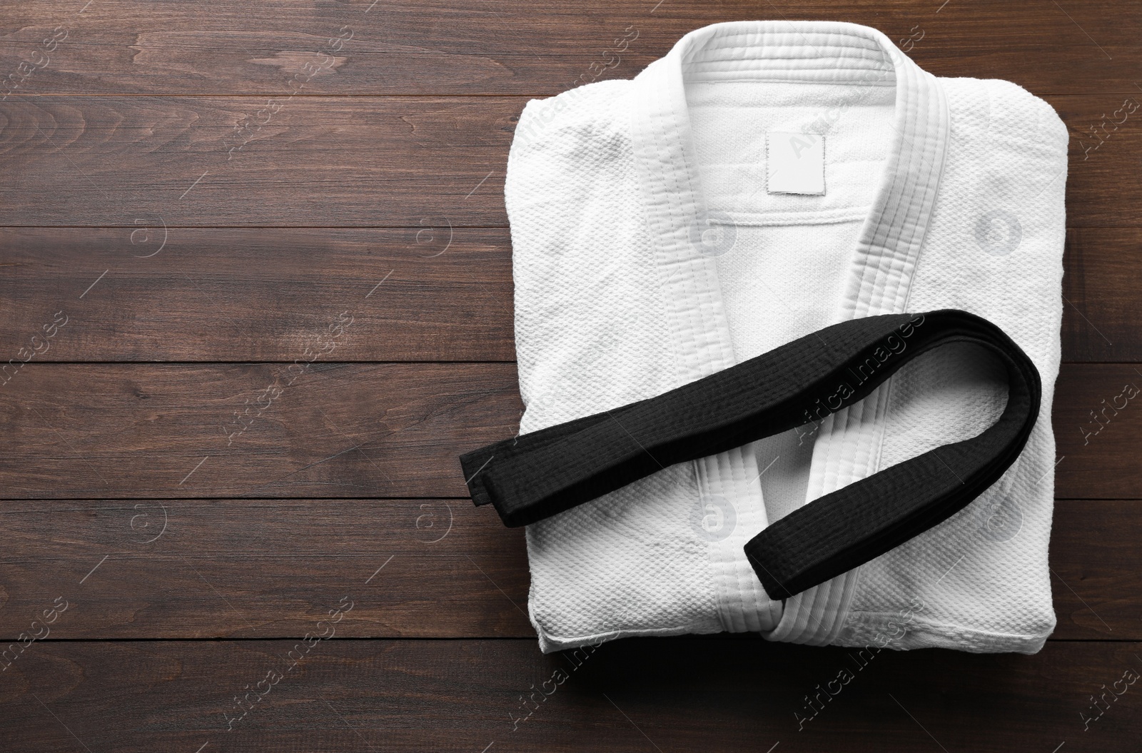 Photo of Martial arts uniform and black belt on wooden background, top view. Space for text