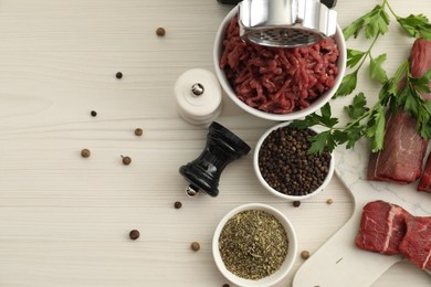 Meat grinder, beef, parsley and spices on white wooden table, flat lay. Space for text