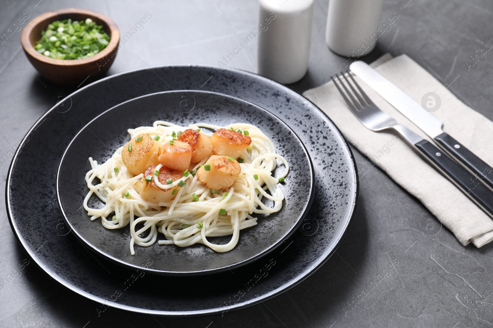 Photo of Delicious scallop pasta with green onion served on grey table