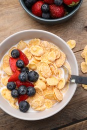 Photo of Bowl of tasty crispy corn flakes with milk and berries on wooden table, flat lay