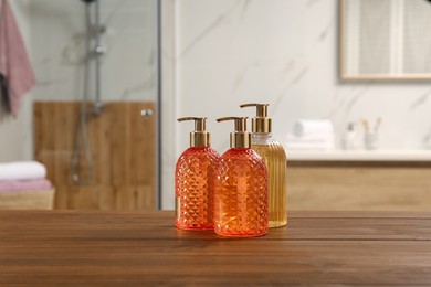 Photo of Different glass dispensers with liquid soap on wooden table in bathroom