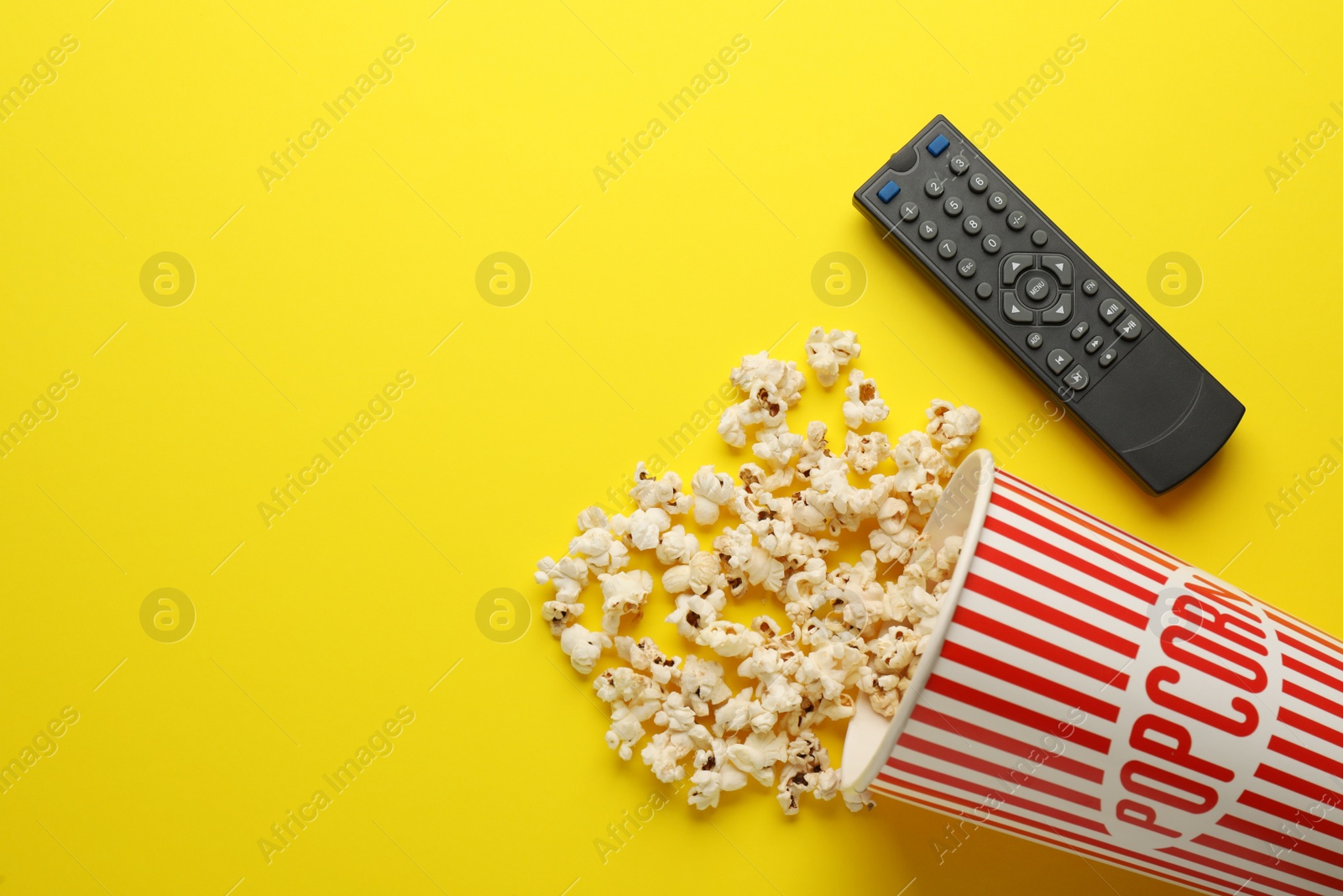 Photo of Remote control and cup of popcorn on yellow background, flat lay. Space for text