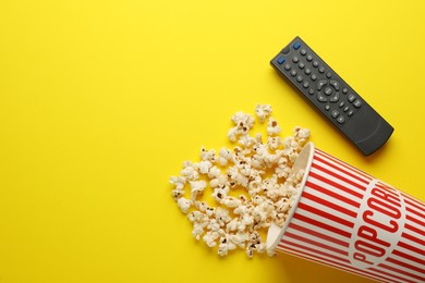 Photo of Remote control and cup of popcorn on yellow background, flat lay. Space for text