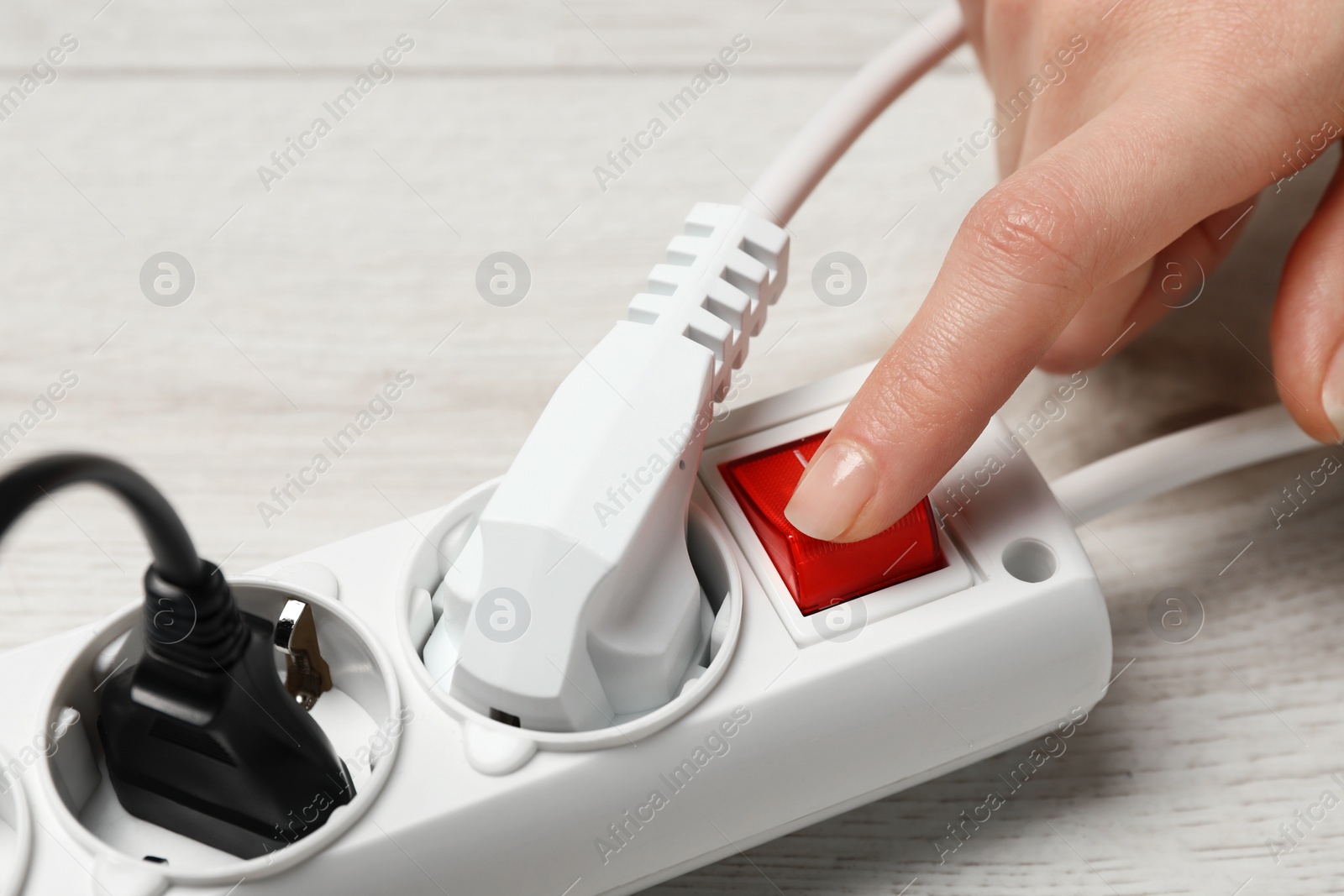 Photo of Woman pressing button of power strip on white wooden floor, closeup. Electrician's equipment