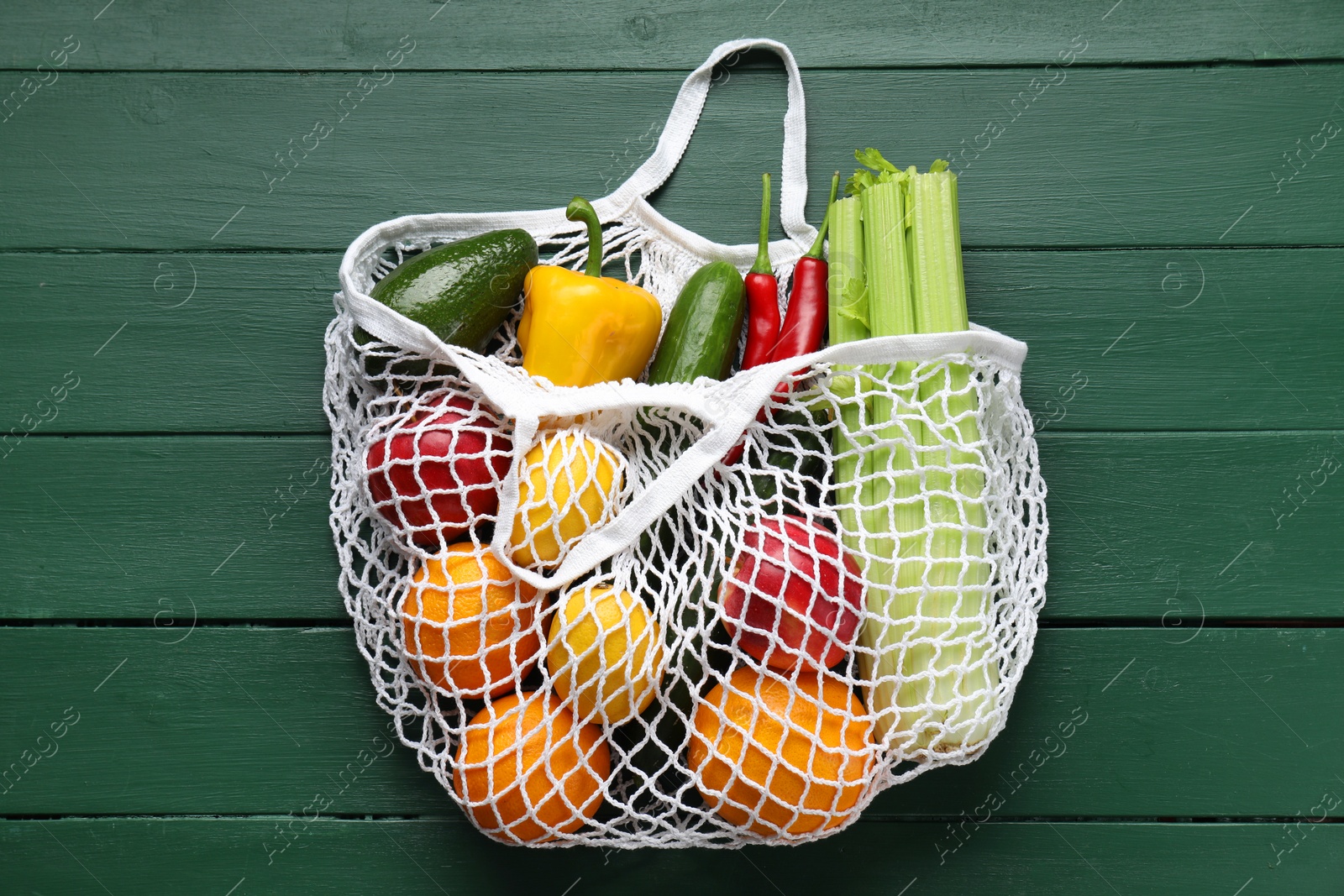 Photo of String bag with different vegetables on green wooden table, top view