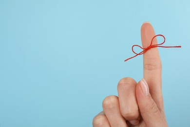 Photo of Woman showing index finger with tied red bow as reminder on light blue background, closeup. Space for text