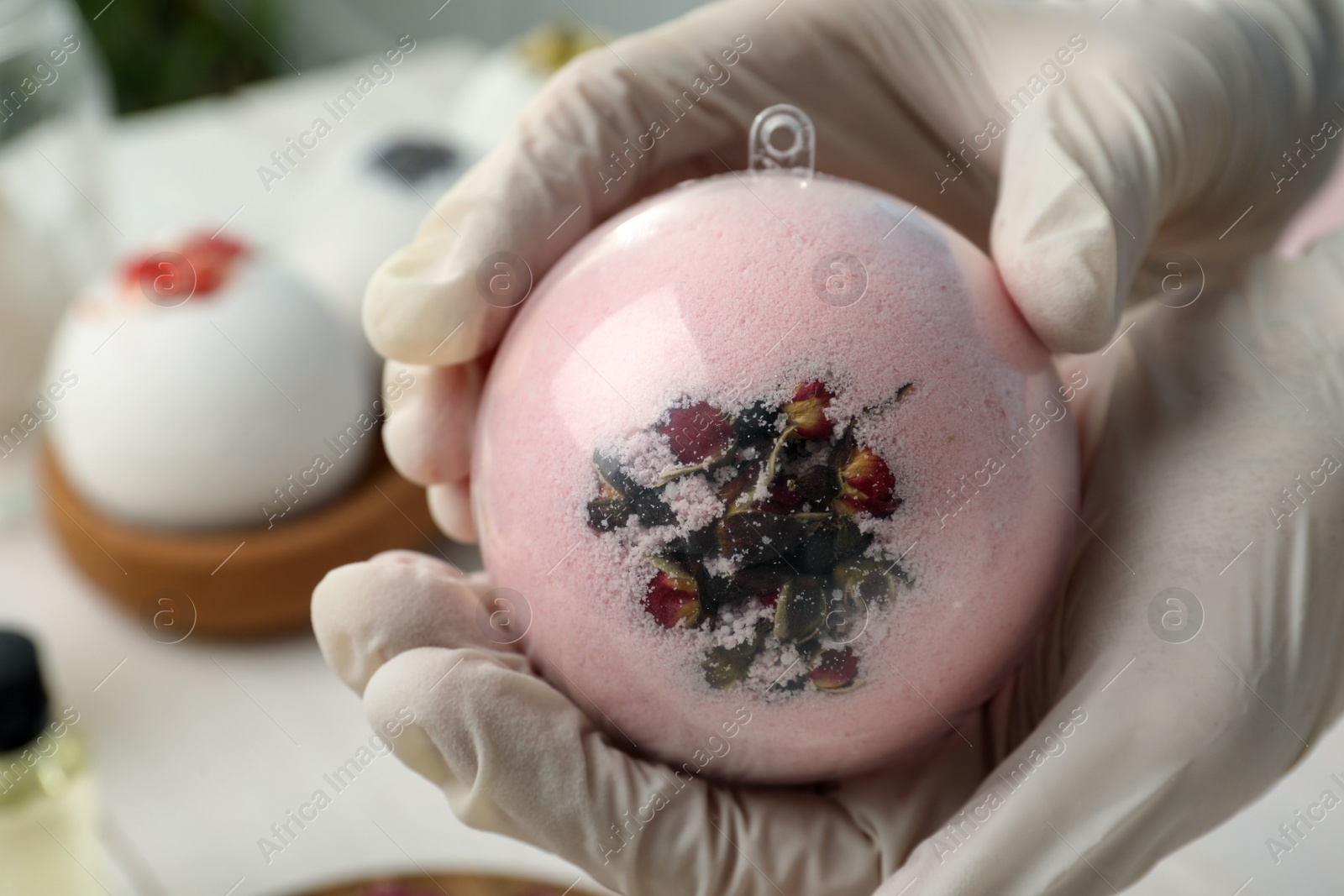 Photo of Woman in gloves making bath bomb at white table , closeup