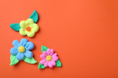 Photo of Colorful flowers with leaves made from play dough on orange background, flat lay. Space for text