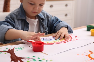 Photo of Little boy painting with finger at wooden table indoors, focus on hands