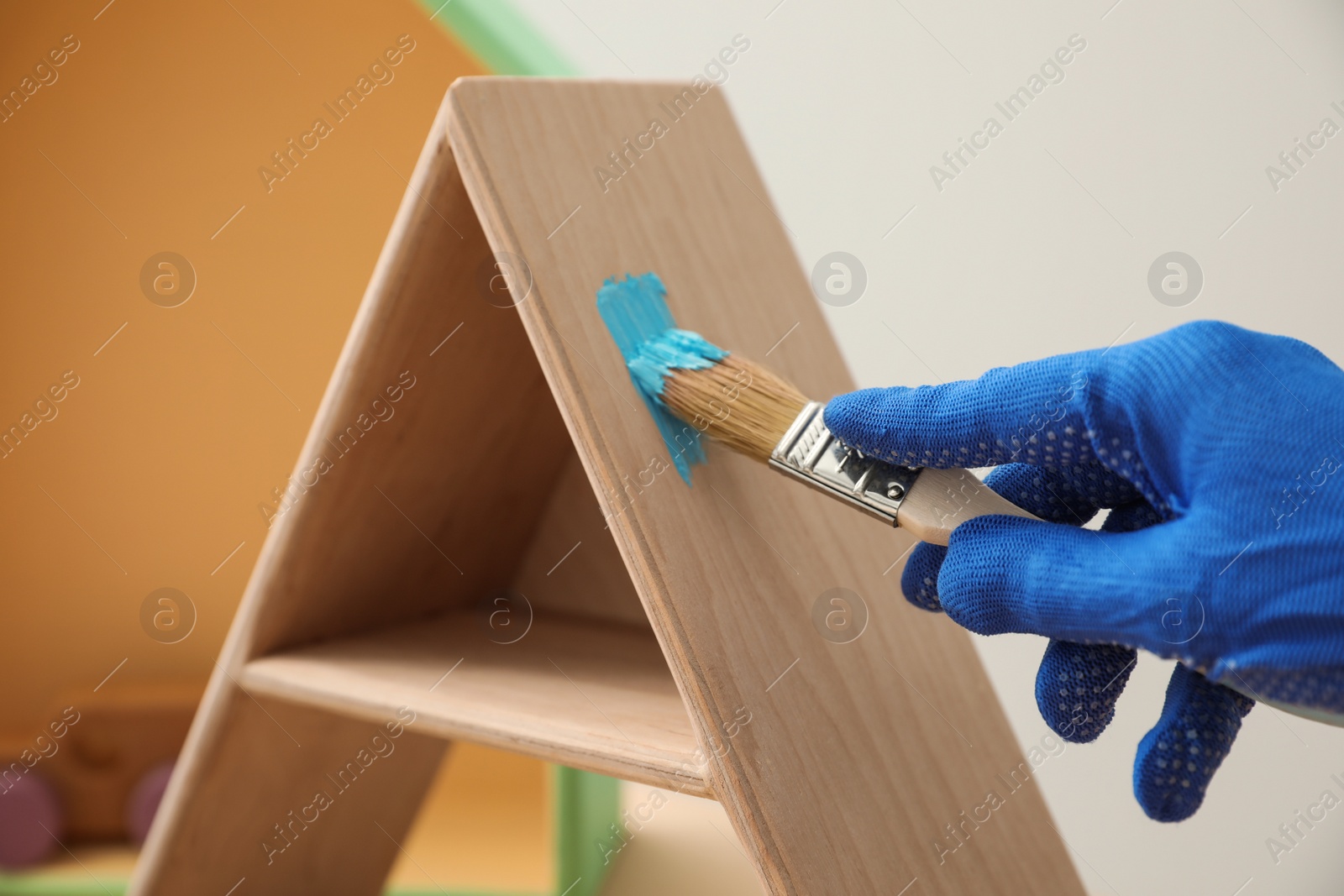 Photo of Decorator painting pyramid shaped shelf with brush, closeup. Interior element