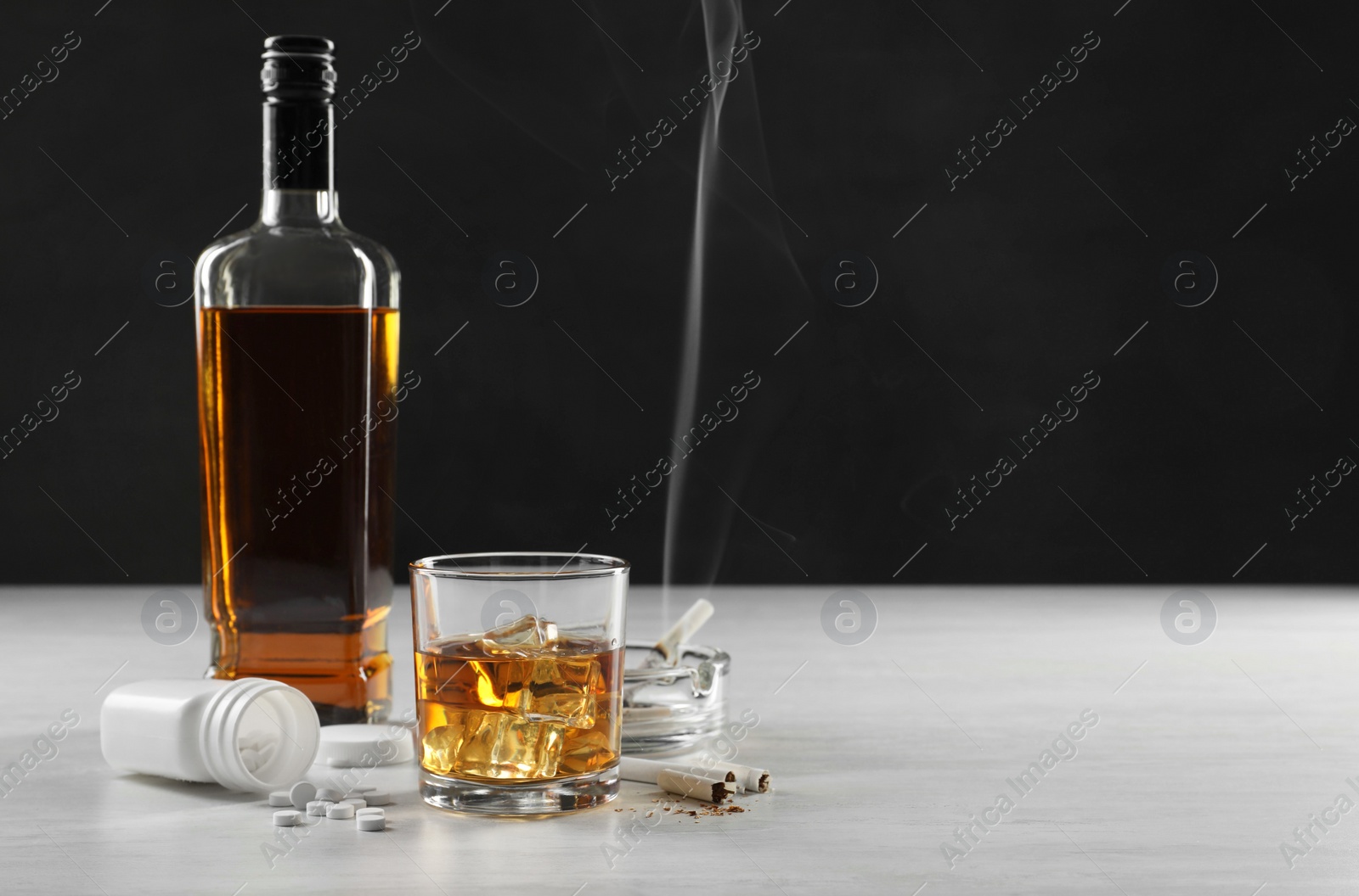 Photo of Alcohol and drug addiction. Whiskey in glass, bottle, cigarettes and pills on white table, space for text