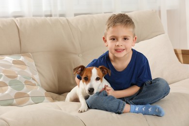 Photo of Little boy with his cute dog on sofa at home, space for text. Adorable pet