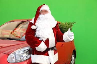 Authentic Santa Claus near car with fir tree and presents against green background
