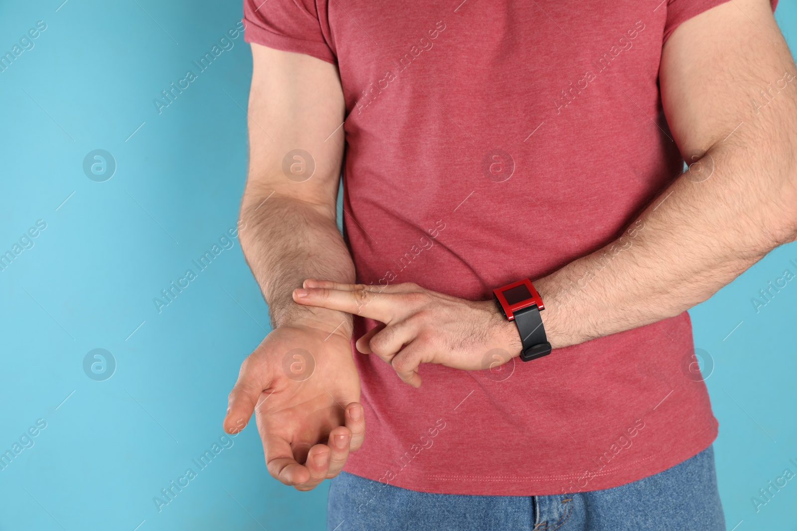 Photo of Young man checking pulse on color background, closeup
