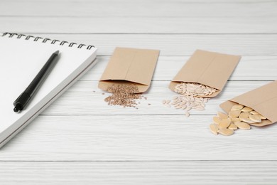 Many different vegetable seeds and notebook on white wooden table