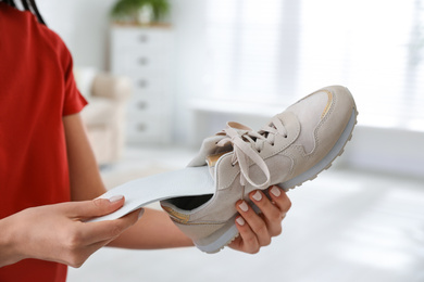 Photo of Woman putting orthopedic insole into shoe at home, closeup