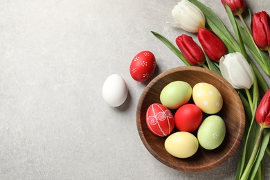 Photo of Flat lay composition of painted Easter eggs and spring flowers on light background, space for text