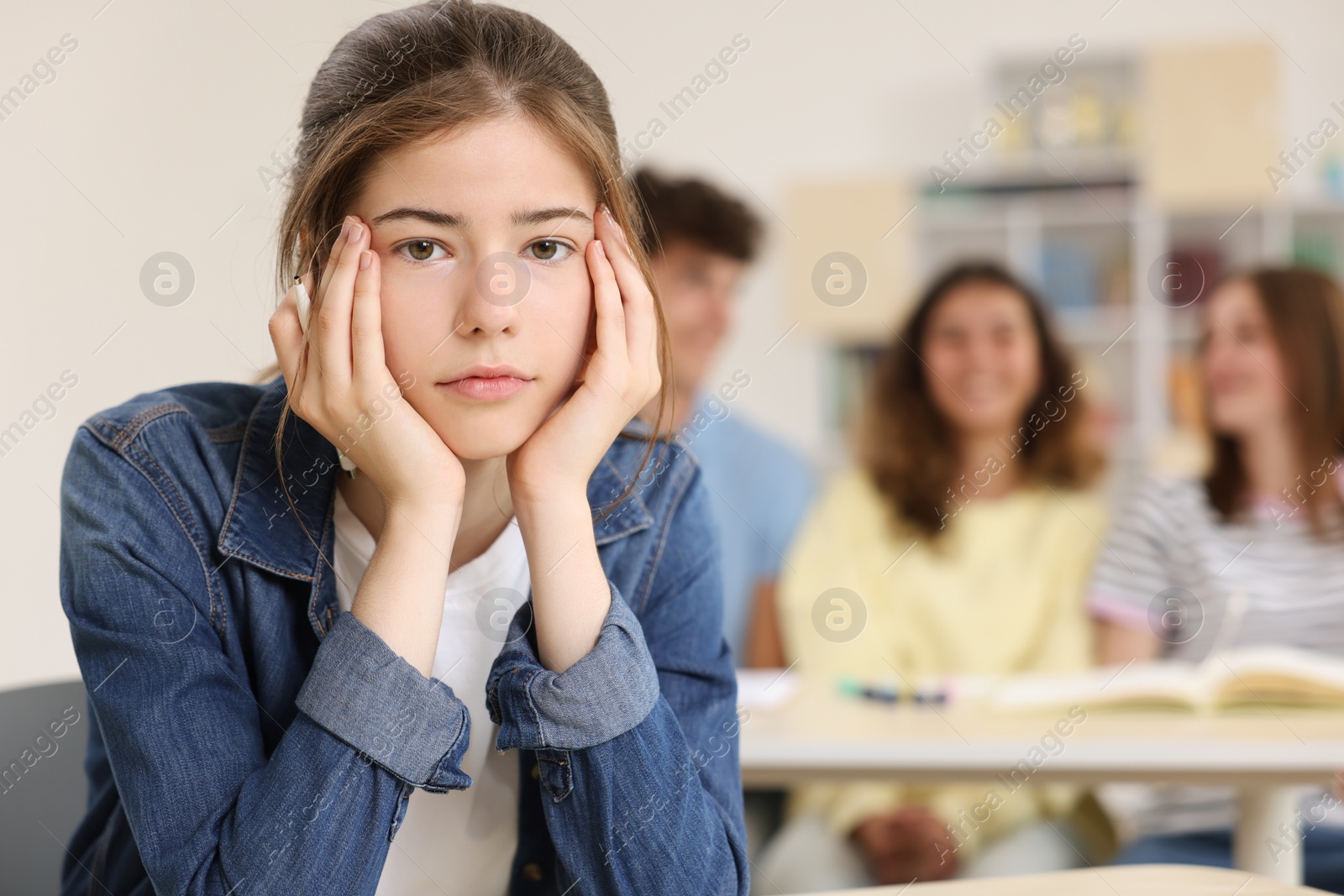 Photo of Teen problems. Lonely girl sitting separately from other students in classroom