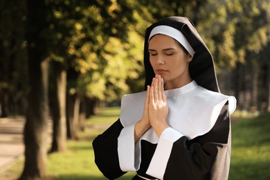 Photo of Young nun with hands clasped together praying in park, space for text