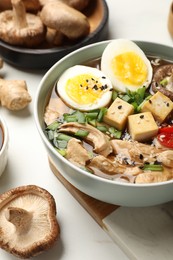 Photo of Bowl of delicious ramen and ingredients on white table. Noodle soup