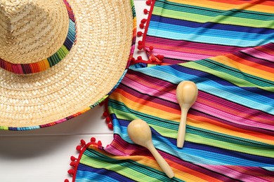 Mexican sombrero hat, maracas and colorful poncho on white wooden background, flat lay