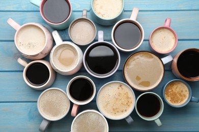 Many cups of different coffee drinks on light blue wooden table, flat lay