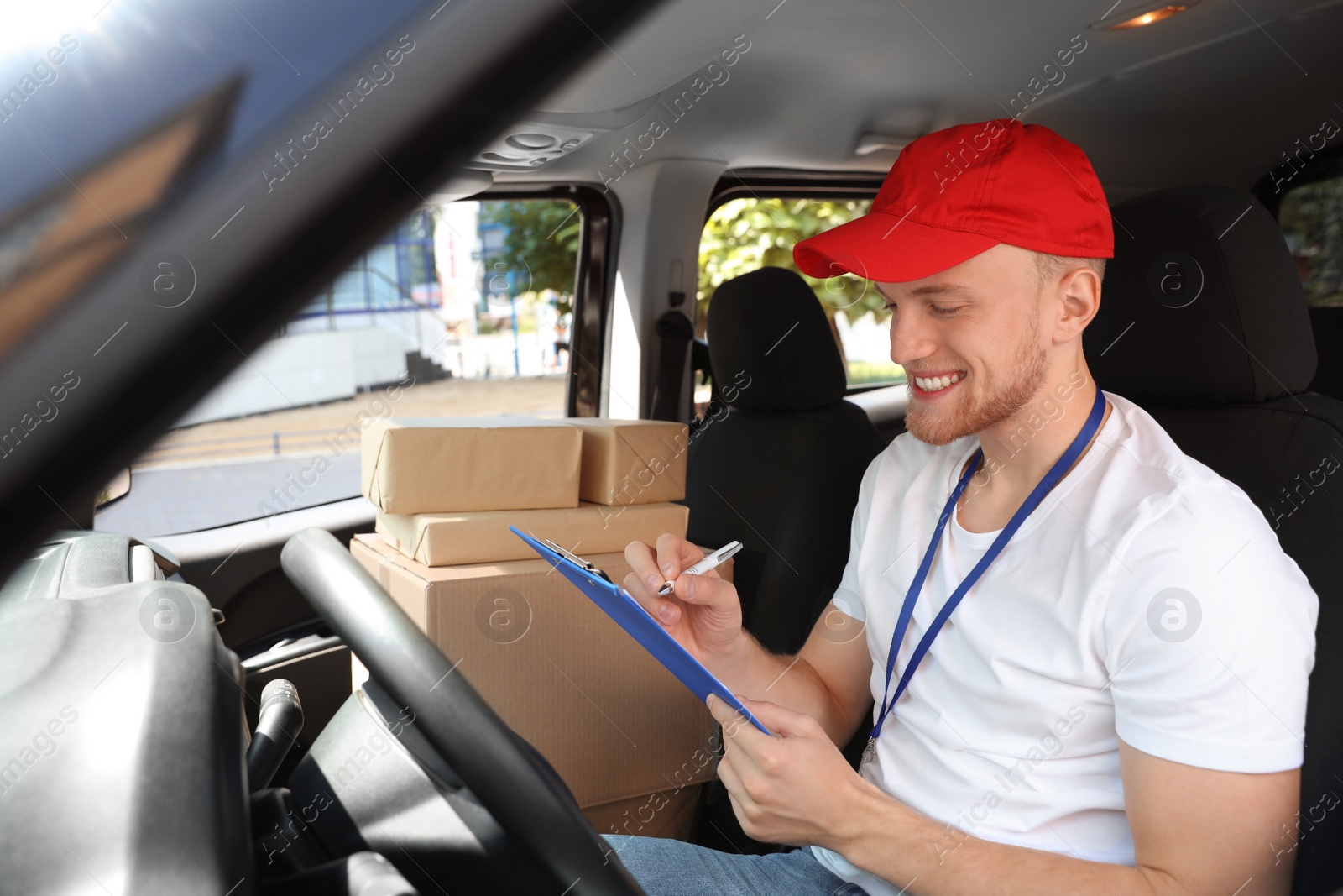 Photo of Young courier with clipboard and parcels in delivery car