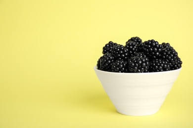 Photo of Fresh ripe blackberries in bowl on yellow background. Space for text