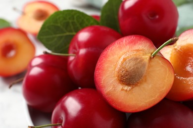 Delicious ripe cherry plums with leaves on table, closeup