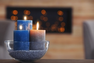 Photo of Bowl with burning candles on table against blurred background. Space for text
