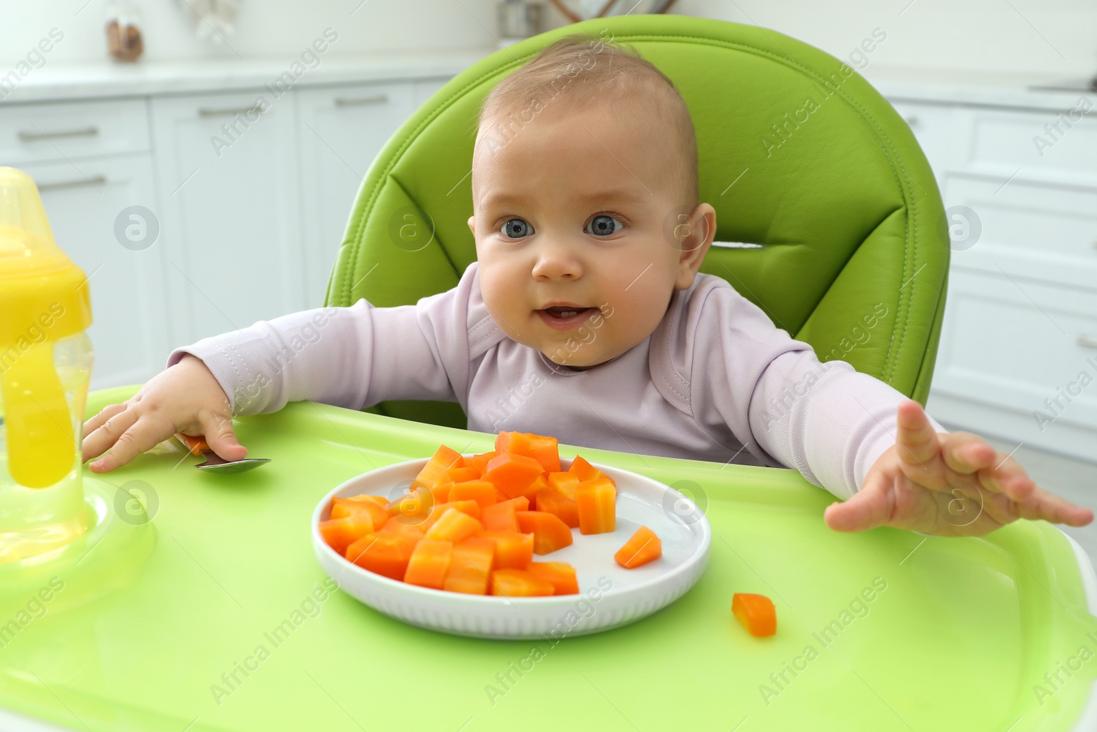 Photo of Cute little baby eating carrot at home, focus on plate