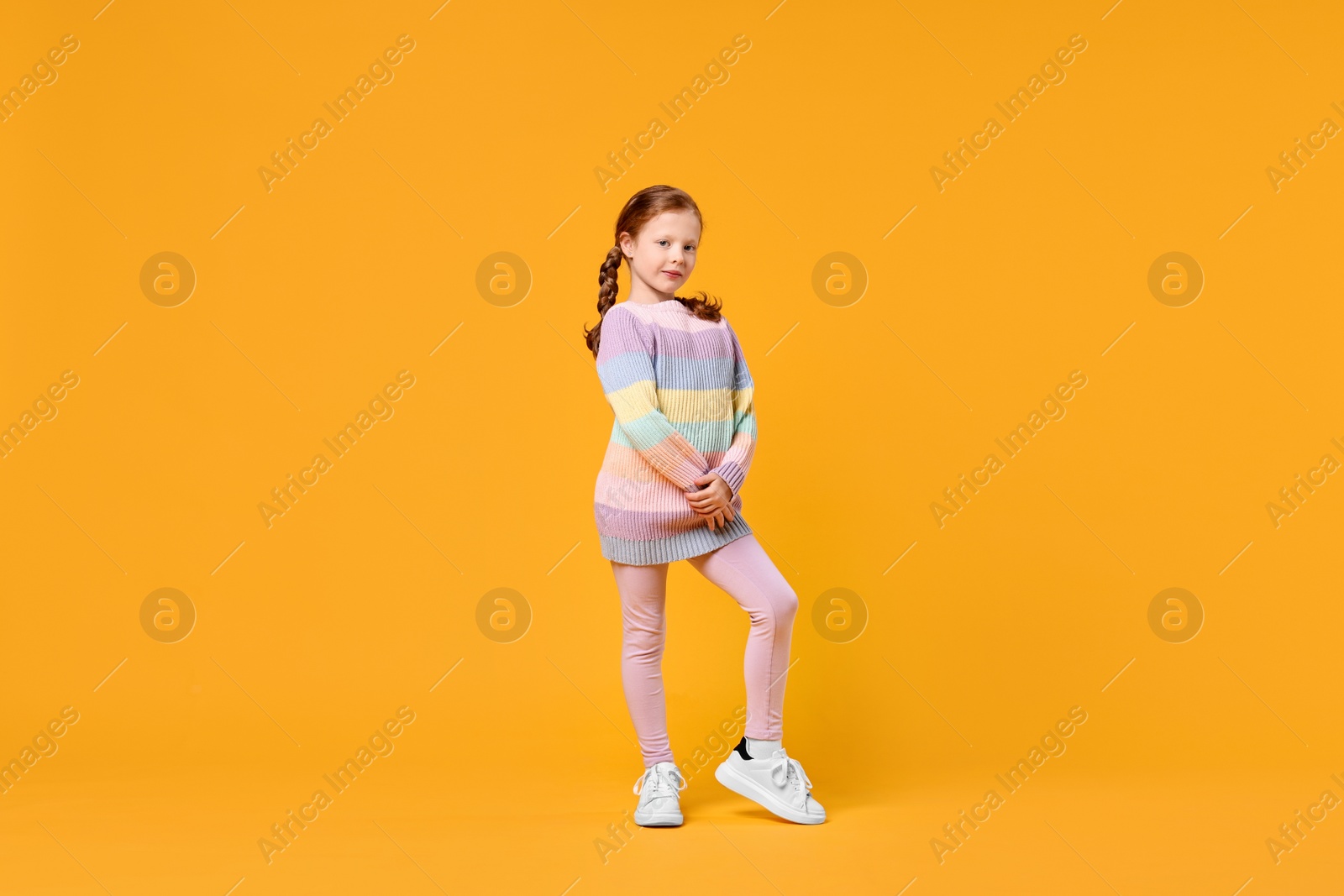 Photo of Cute little girl dancing on orange background